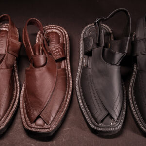 Top view of two pairs of traditional Peshawari chappals—one in rich brown leather, the other in matte black—displayed side by side on a dark surface to highlight stitching, design, and craftsmanship.