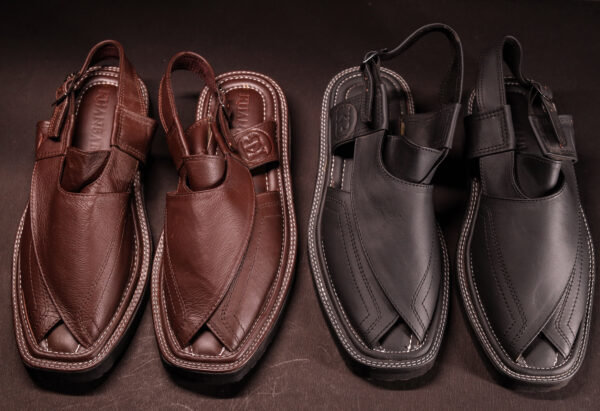 Top view of two pairs of traditional Peshawari chappals—one in rich brown leather, the other in matte black—displayed side by side on a dark surface to highlight stitching, design, and craftsmanship.