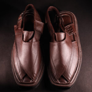 Top view of a pair of handcrafted brown leather Peshawari chappals featuring a traditional cross-strap design and detailed stitching, placed on a dark textured background.