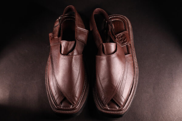 Top view of a pair of handcrafted brown leather Peshawari chappals featuring a traditional cross-strap design and detailed stitching, placed on a dark textured background.
