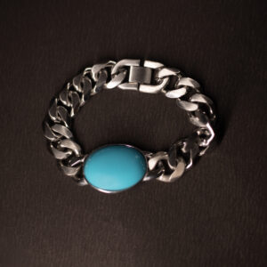 A silver chain bracelet with a bold, oval turquoise stone centrepiece, displayed on a dark textured background.