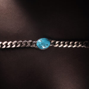 Flat-lay image of a silver Cuban link bracelet with a marbled turquoise stone centrepiece, placed on a dark textured background with dramatic lighting.